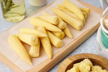 Wooden board with tasty canned corn cobs on light background