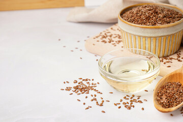 Bowl with flax oil and spoon of seeds on white background