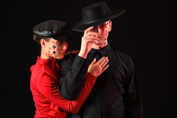 Young couple with drawn card suits on their faces against dark background
