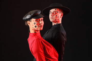 Young couple with drawn card suits on their faces against dark background