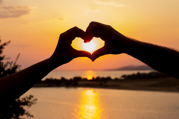 man and woman hands making heart shape with sunset background