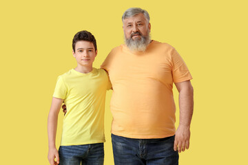 Happy grandfather with his cute grandson on yellow background