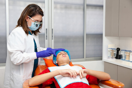 Skin lesion removal procedure. Dermatologist carrying out a removal of benign skin lesion on the face of a young male patient.
