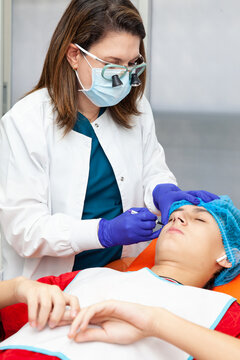 Skin lesion removal procedure. Dermatologist carrying out a removal of benign skin lesion on the face of a young male patient.