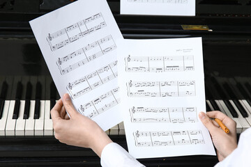 Young woman holding note sheets near piano