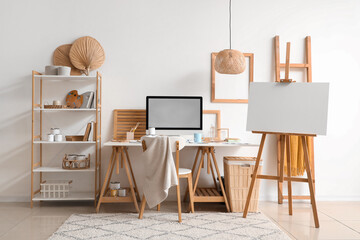 Workplace with modern computer and canvas on easel in office