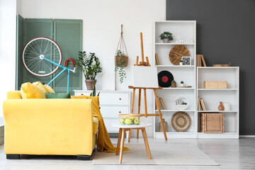 Interior of stylish living room with yellow sofa, coffee table, canvas and bicycle