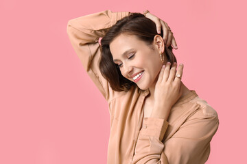 Beautiful young happy woman wearing stylish golden jewelry on pink background