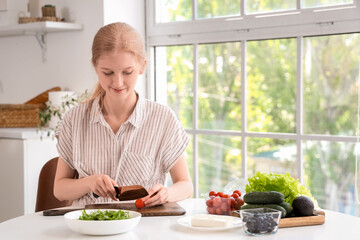 Young woman cutting tomatoes for salad with feta cheese in kitchen
