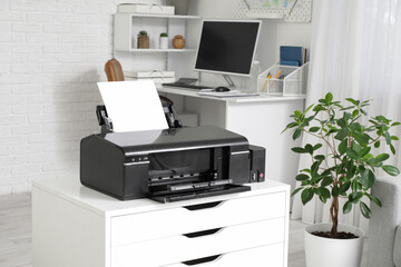 Modern printer on chest of drawers and workplace in stylish office