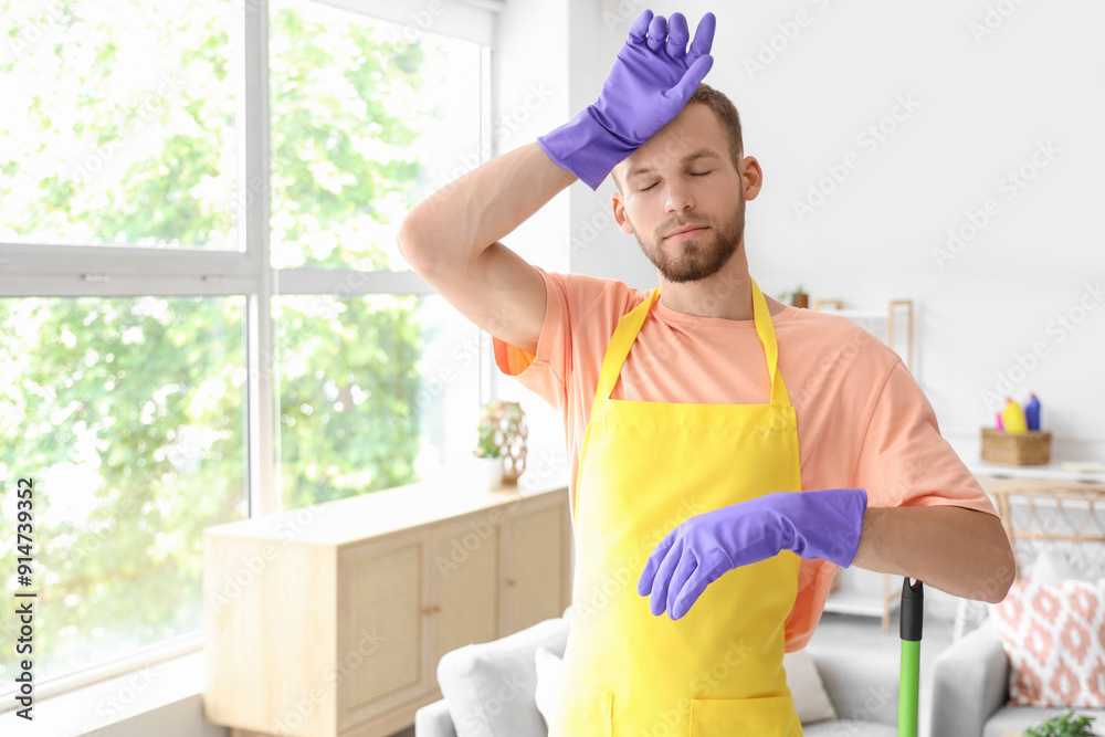 Poster tired male janitor in rubber gloves in light room