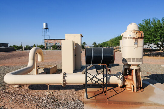 Agricultural groundwater vertical pump system with exposed piping, motor, and control box on desert terrain, supporting rural irrigation infrastructure and municipal water delivery operations
