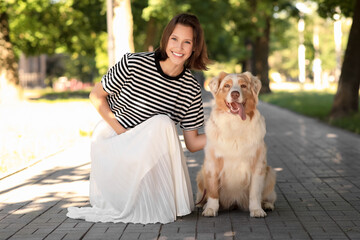 Beautiful young woman with cute Australian Shepherd dog sitting in park