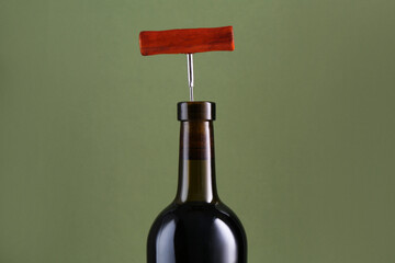 Wine bottle with corkscrew on olive background, closeup