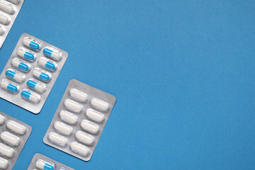 Different antibiotic pills in blisters on light blue background, flat lay. Space for text