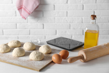 Raw dough balls, eggs, oil, rolling pin and kitchen scale on white wooden table