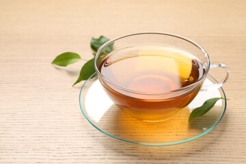 Refreshing green tea in cup and leaves on wooden table, closeup