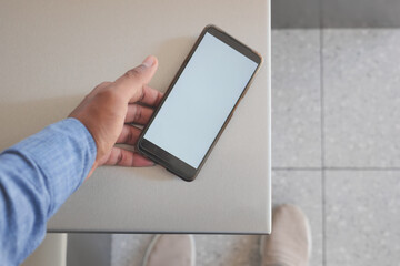 A hand is holding a smartphone over a table where the screen is blank and empty