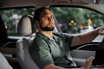 Man driving a car with a focused expression in a city setting at night