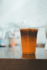 Tasty refreshing drink with coffee and orange juice in plastic cup on wood table.