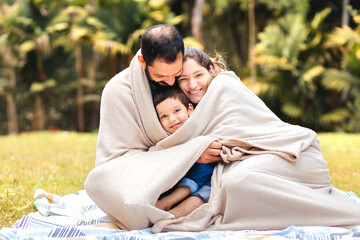 Brazilian family wrapped in a cozy blanket, smiling and enjoying time outdoors. Capturing warmth,...