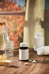 Creative scene for advertising with pharmacy theme. A medicine bottle with white label displayed on wooden table with glass cup, bottles and daily medicine box. Behind is with with autumn landscape