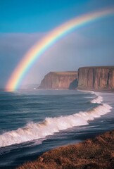 Fototapeta premium A brilliant rainbow arching over a coastal landscape, with waves crashing on the shore and cliffs in the distance, capturing the harmony of nature
