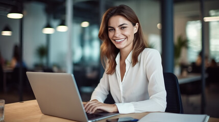 Fototapeta premium A happy business woman working on her laptop in an office, sitting at her desk with papers and documents around her.
