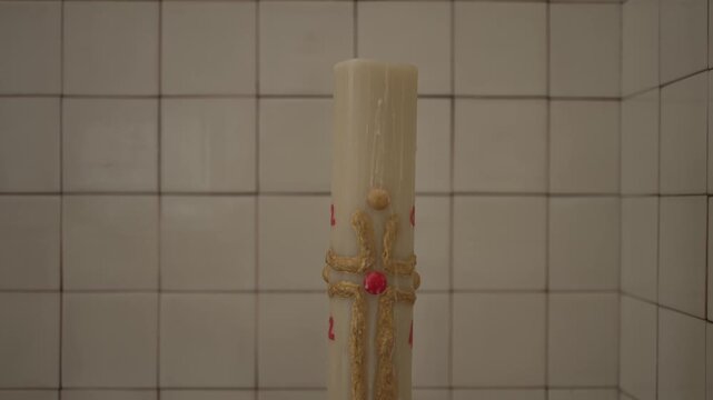 Intricate Paschal candle with gold detailing against tiled background, symbolizing faith