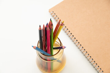 Colored pencils with notebook on white background.
School and office supplies image.
