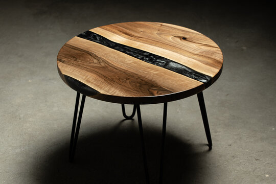Expensive vintage furniture. The table is covered with epoxy resin and varnished. Luxury quality wood processing. Wooden table on a dark background. A black epoxy river in a round tree slab.	