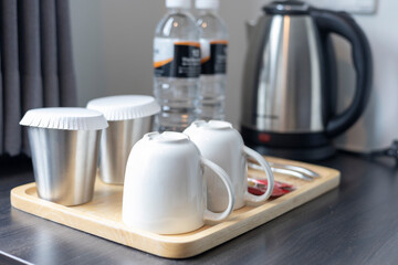 Modern Kitchen Setup: Mugs and Cups Neatly Arranged on a Wooden Tray Next to a Silver Kettle and Water Bottles, Creating a Clean and Organized Beverage Station on the Countertop