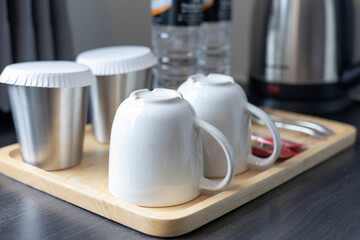 Modern Kitchen Setup: Mugs and Cups Neatly Arranged on a Wooden Tray Next to a Silver Kettle and Water Bottles, Creating a Clean and Organized Beverage Station on the Countertop