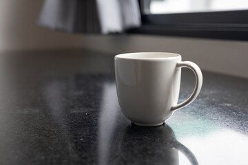 Minimalist White Ceramic Coffee Cup: Empty and Clean, Resting on a Table with Morning Light Reflecting Through a Window.