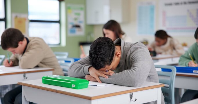 Exam, boy and tired on desk with stress, overwhelmed and brain fog in classroom. Student, depression and overthinking in test with anxiety, burnout and mental health fatigue in high school lesson