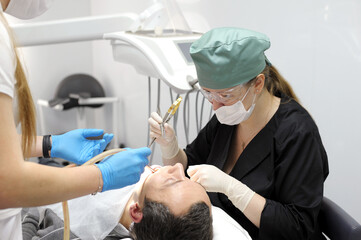 Closeup woman patient. Carious tooth treatment at dental clinic office. Nurse, doctor hand. Dentist making teeth cleaning, treating and canal filling. assistant spaying mouth, using saliva ejector