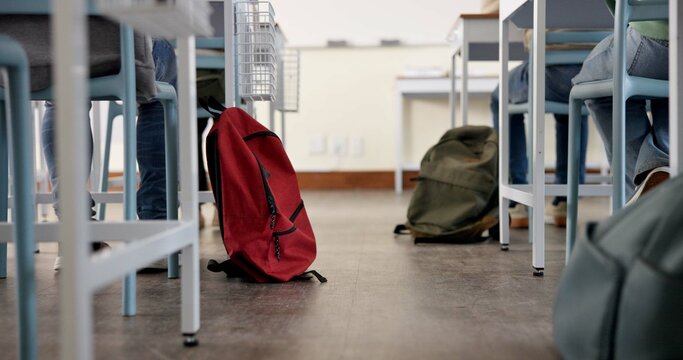 Classroom, backpack and education in school, students and low angle of learning of kids in academy. Desk, legs and children with scholarship, studying and writing of practice exam, bag and knowledge - Powered by Adobe