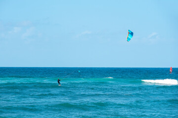 Kite surfer rides waves under clear blue sky on sunny day at beach