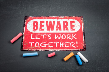 Let's Work Together . Beware sign with text and colored pieces of chalk on a dark chalkboard background