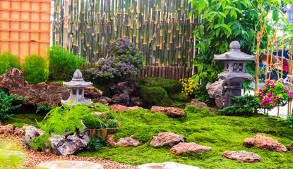 Minimal Japanese garden in home with small stone lantern and bamboo fountain and moss and flowers.

