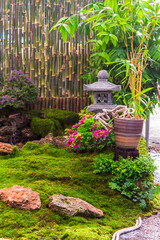 Minimal Japanese garden in home with small stone lantern and bamboo fountain and moss and flowers.

