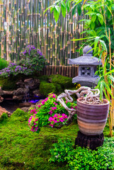 Minimal Japanese garden in home with small stone lantern and bamboo fountain and moss and flowers.

