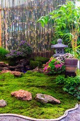 Minimal Japanese garden in home with small stone lantern and bamboo fountain and moss and flowers.

