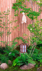 Minimal Japanese garden in home with small stone lantern and bamboo fountain and moss and flowers.

