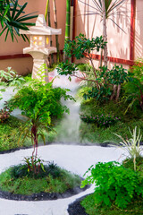 Minimal Japanese garden in home with small stone lantern and bamboo fountain and moss and flowers.

