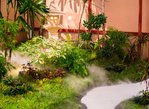 Minimal Japanese garden in home with small stone lantern and bamboo fountain and moss and flowers.

