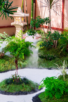 Minimal Japanese garden in home with small stone lantern and bamboo fountain and moss and flowers.

