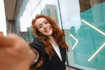 Fototapeta premium Young Woman With Red Hair Smiles and Poses Playfully at Urban Location During Cloudy Day