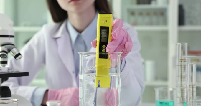 Researcher immerses pH meter into beaker of clear water. Scientist monitors digital readout noting changes revealing water pH level in lab