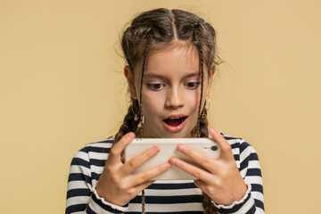 Happy excited young preteen child girl kid player celebrate victory enthusiastically playing racing drive simulator or shooter video games on smartphone. Teenager children isolated on beige background